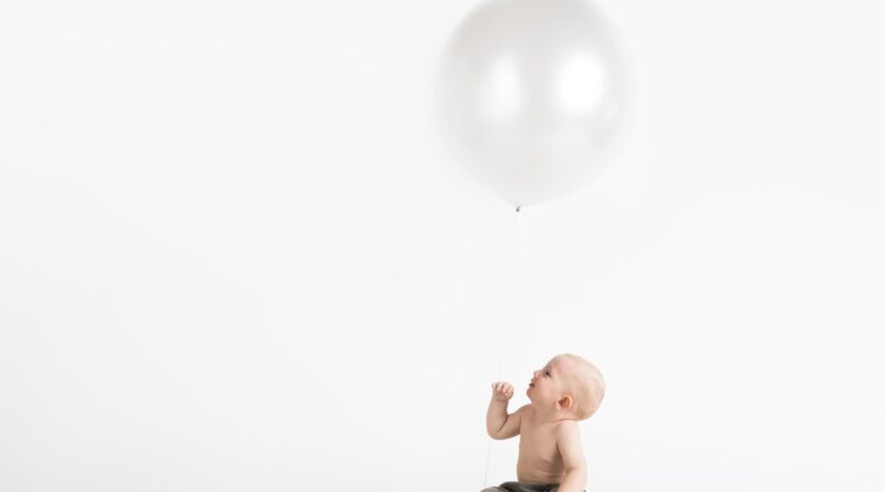 boy sitting wearing black pants under white balloon