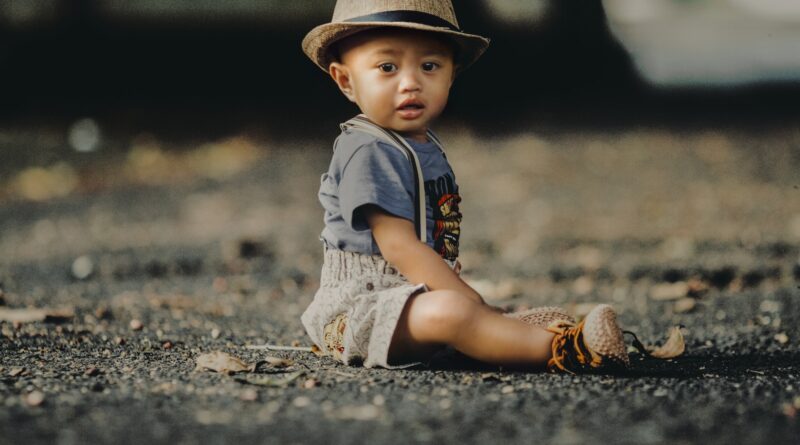 Child In Grey Shorts Sitting On Road